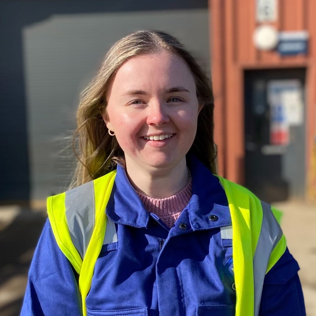 KR Group apprenticeship employee, smiling, and wearing blue overalls and a hi-vis vest, while standing in the yard at KR Group in Aberdeenshire.