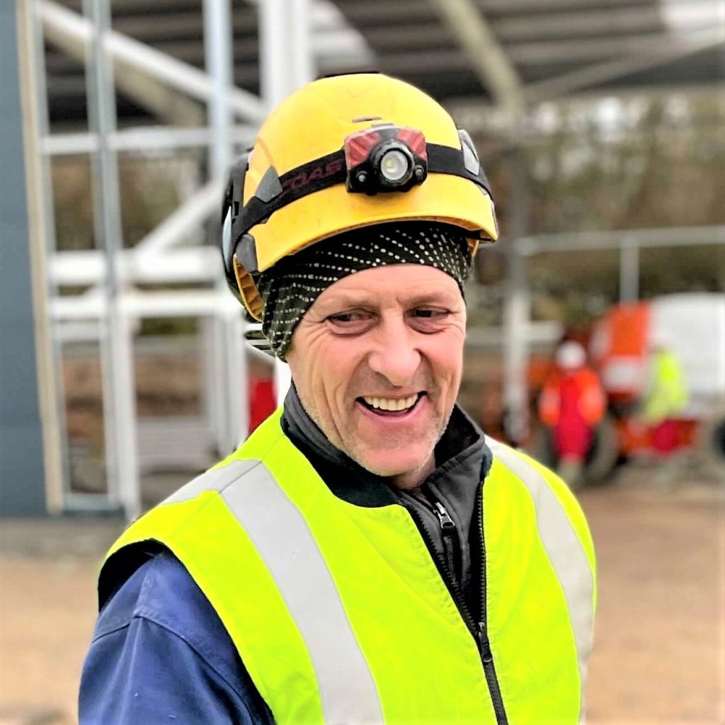 Image of smiling KR Group safety net site worker on a construction site, wearing a high-vis vest and hard hat.