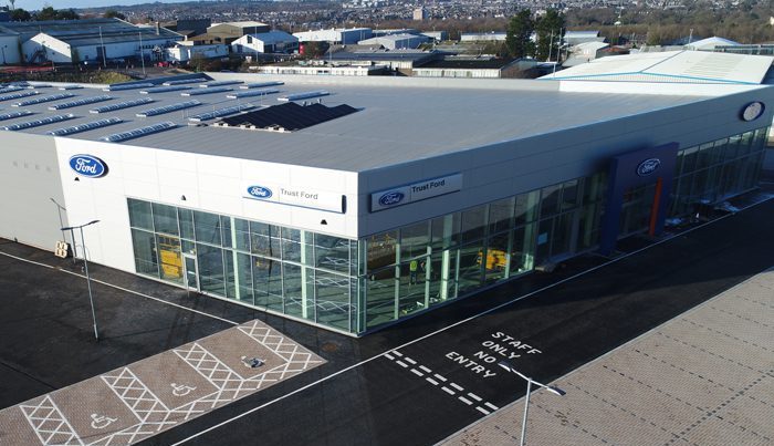 A sunny, aerial view of the TrustFord garage showroom in Aberdeen, with steel construction and cladding installation by KR Group. Showing the Ford logo and entrance to the building.