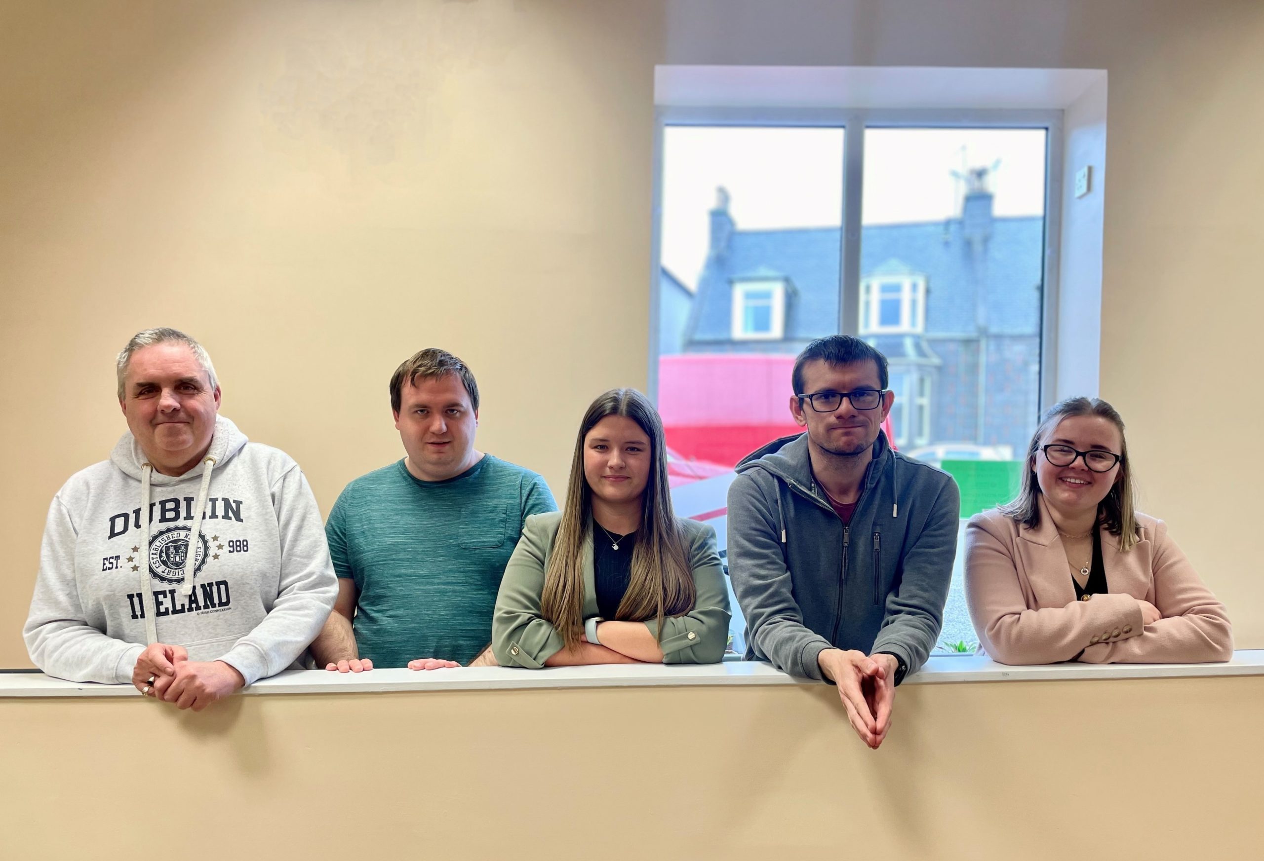 Fundraising team members from KR Group posing next to a window with Grampian Opportunities service users.