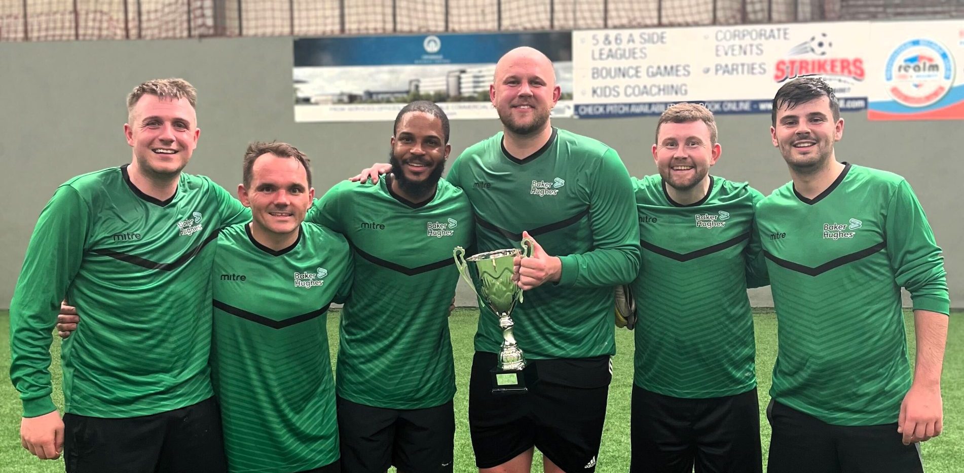 KR Group Charity Football Tournament winning team, Baker Hughes, posing with trophy on pitch at Strikers Indoor Football in Aberdeen.