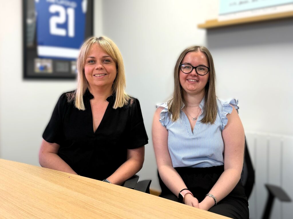 From left to right: Jayne Simpson, Head of Finance at KR Group and Lauren Moroney, Business Operations Supervisor, sitting in the board room smiling for the camera.